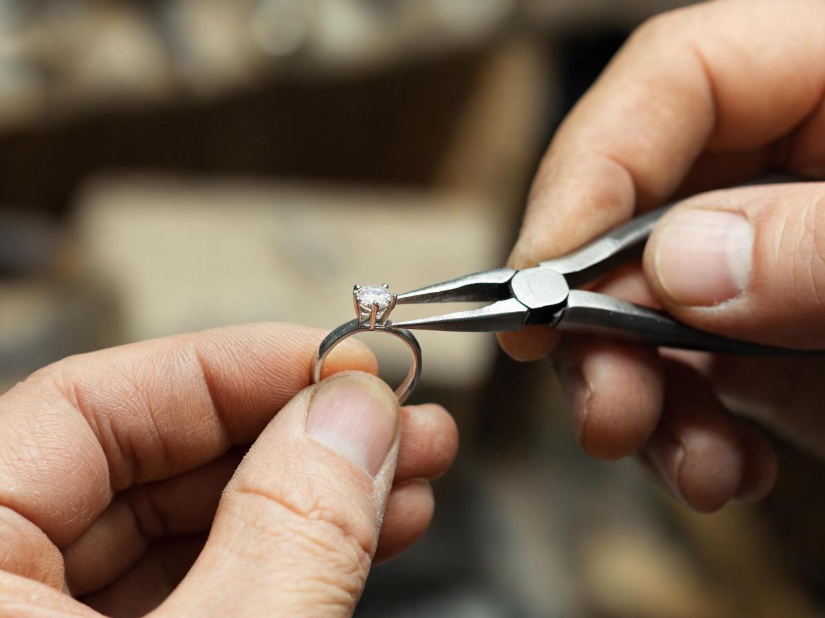 A close-up of a jeweler’s hands adjusting a stone setting on a silver ring prototype with precision tools