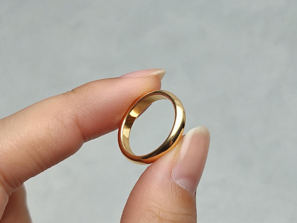 Close-up of hands inspecting a thin gold ring sample, checking the inner edge and finish quality against a neutral work surface